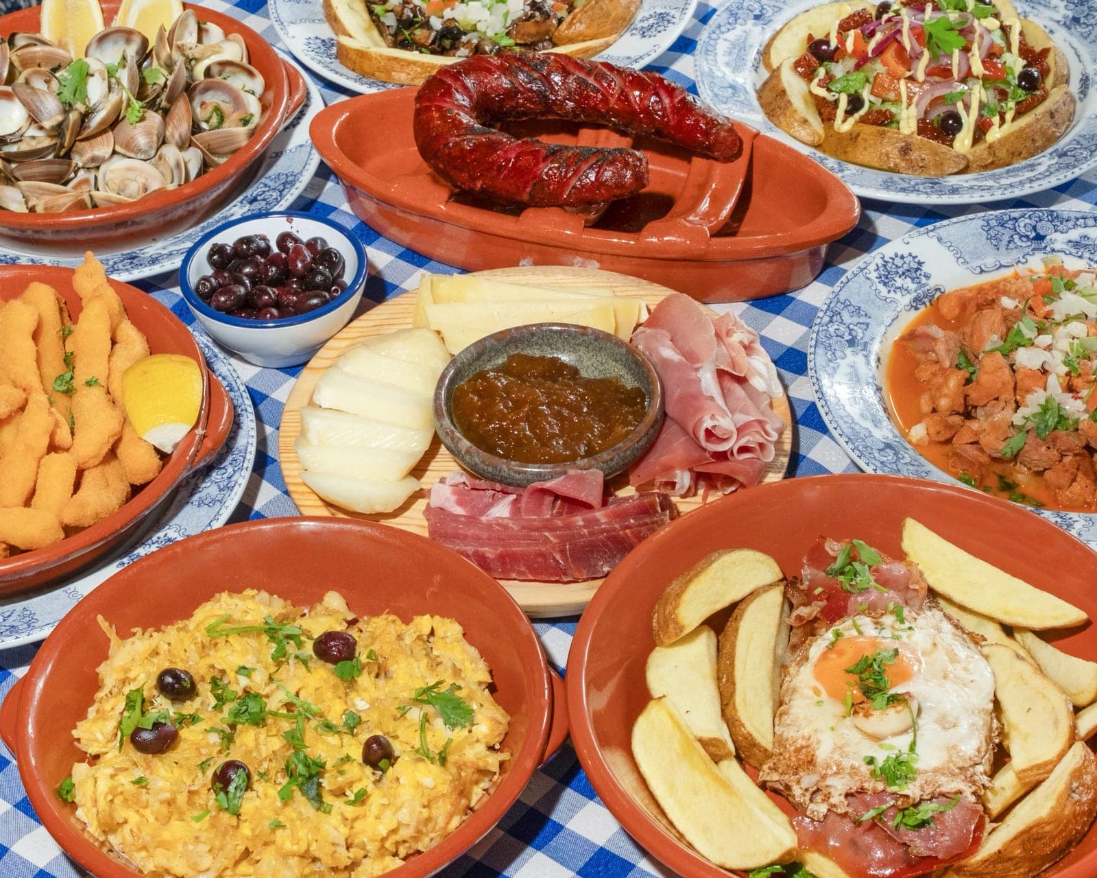 Mesa posta com pratos tradicionais portugueses em barro, sobre toalha axadrezada azul e branca